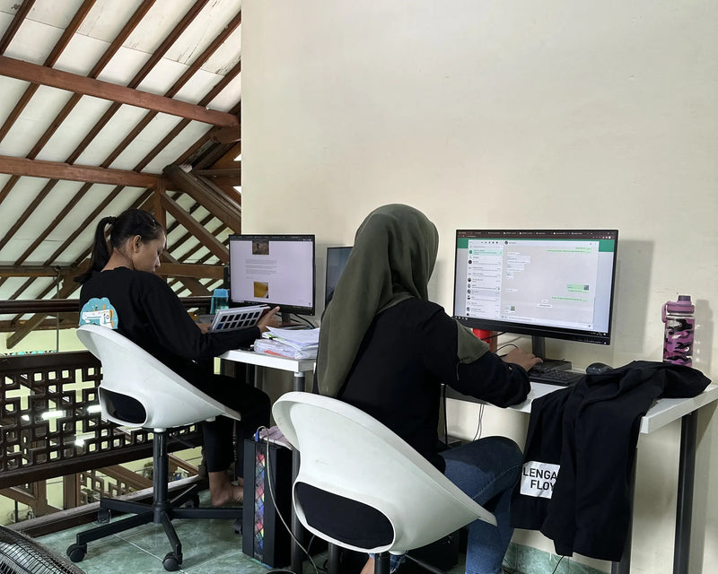 Two people working on computers at a desk with a wooden roof structure in the background.