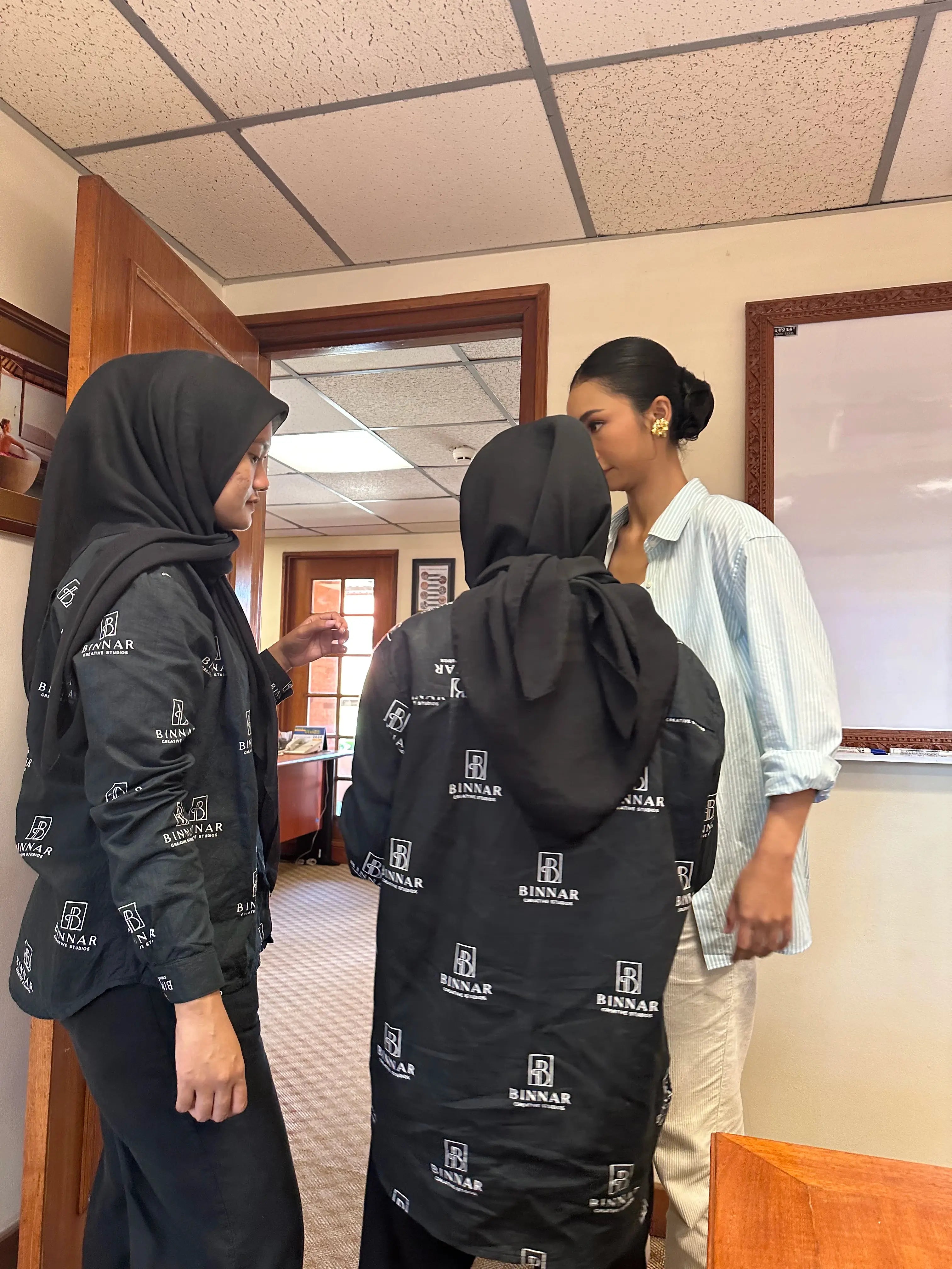 Three women in a room, two wearing black hoodies with logos and one in a light shirt.